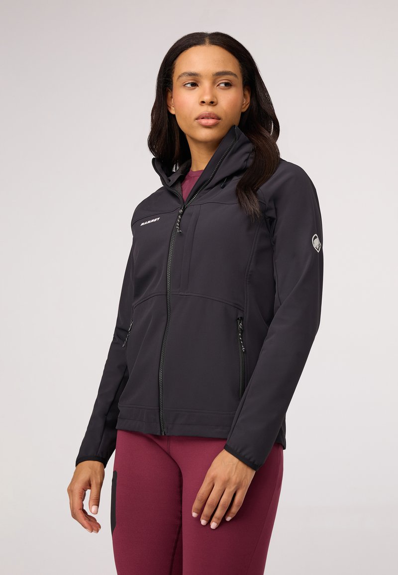 Black softshell jacket with a zip front, high collar, and two side pockets. Features a logo on the chest and a textured finish.