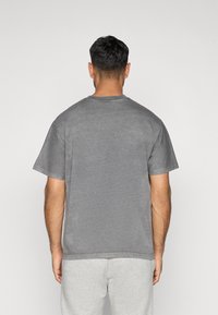 T-shirt de algodão cinza com mangas curtas e decote redondo, apresentando uma textura ligeiramente desbotada e um corte descontraído, vista pela parte de trás.