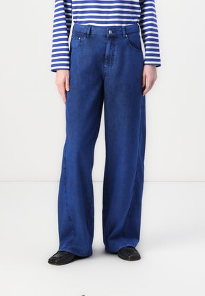 Blå vid benjeans laget av denim, med glidelås, frontlommer og synlige sømdetaljer. Kombinert med en stripete langermet skjorte.