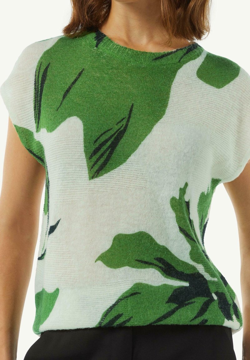 Kevyt, lyhythihainen neulepaita valkoisena, jossa on suuria vihreitä lehtikuvioita ja tummanvihreitä yksityiskohtia. Paita on varustettu pyöreällä kaula-aukolla ja rentolla istuvuudella.