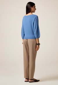 Pull en tricot bleu avec des manches trois-quarts et un large décolleté, associé à un pantalon beige taille haute et des sandales plates noires.