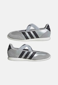 Coppia di sneakers slip-on argento e grigie con strisce nere e fascette elastiche incrociate, suole bianche piatte, vista laterale.