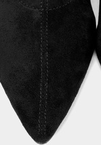 Czarne zamszowe buty z noskiem w szpic, z kontrastowym przeszyciem wzdłuż szwów, o gładkiej fakturze i smukłym kształcie.