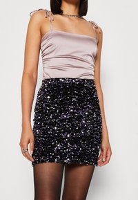 Haut en satin avec des bretelles fines, présentant une silhouette ajustée. La jupe pailletée noire et violette a une surface texturée et brillante.