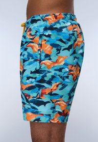 Bañador en un vibrante azul, naranja y negro con un patrón abstracto; hecho de tejido ligero con una cinturilla elástica y un bolsillo lateral.