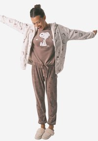 Lettet pyjamakombination bestående af en grå zip-hoodie med tegneserie-mønstre, en brun T-shirt med korte ærmer og Snoopy-print, samt matchende brune bukser.