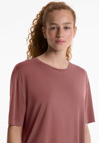 T-shirt rosa a maniche corte, colletto girotondo, con una texture liscia e una vestibilità rilassata, caratterizzato da una leggera drappeggiatura e senza motivi o abbellimenti visibili.
