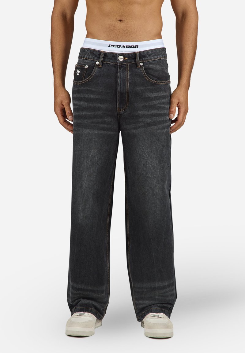 Bredde ben sorte denim jeans med orange syninger, forlommer og knaplukning; båret med hvid PEGADOR talje og cremefarvede sneakers.