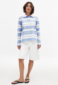 Prúžkovaná polo košeľa s dlhým rukávom v svetlom modrom a bielom prevedení, so klasickým golierom. V kombinácii s bielymi šortkami a čiernymi žabkami.