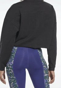 Felpa nera corta con maniche oversize; abbinata a leggings blu con un motivo astratto verde e bianco sui lati.
