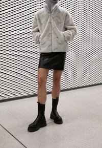 Světle šedá umělá kožešinová bunda volného střihu, kombinovaná s černou koženou mini sukénkou a masivními černými kotníkovými botami. Hladké textury a jednoduchý design.