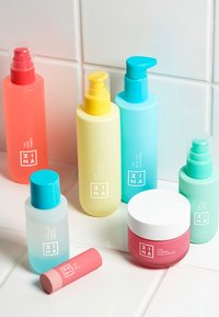 Set med åtte hudpleieprodukter i ulike flasker. Fargene inkluderer rosa, gul, blå og grønn. Har glatte teksturer og etiketter med hvit tekst.