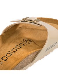 Béžové žabky s texturovanou hnědou semišovou stélkou a lesklým páskem s zlatým sponou. Název značky "palado" vytištěn uvnitř.
