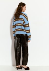 Pulover cu dungi albastre, cu dungi maronii și crem, asortat cu pantaloni din piele neagră cu talie înaltă și sandale din blană neagră.