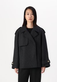 Manteau en laine gris foncé avec un large col, coupe oversize, poches à rabat avant et poignets boutonnés. Texture lisse et design classique.