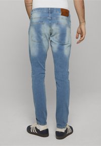 Světlé modré džíny z denimu s úzkým střihem, s hnědou koženou nášivkou na zadní straně, minimálním vyblednutím a standardními kapsami.