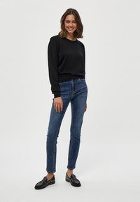 Maglione nero a maniche lunghe con scollo rotondo, abbinato a jeans slim-fit blu scuro e mocassini neri. Texture semplice e liscia. Look casual.