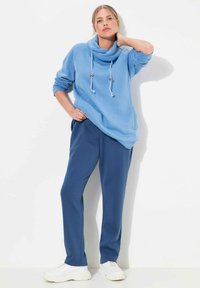 Jasnoniebieski oversizowy sweatshirt z kapturem i kontrastującymi białymi sznurkami, zestawiony z ciemnoniebieskimi spodniami dresowymi i białymi sneakersami.