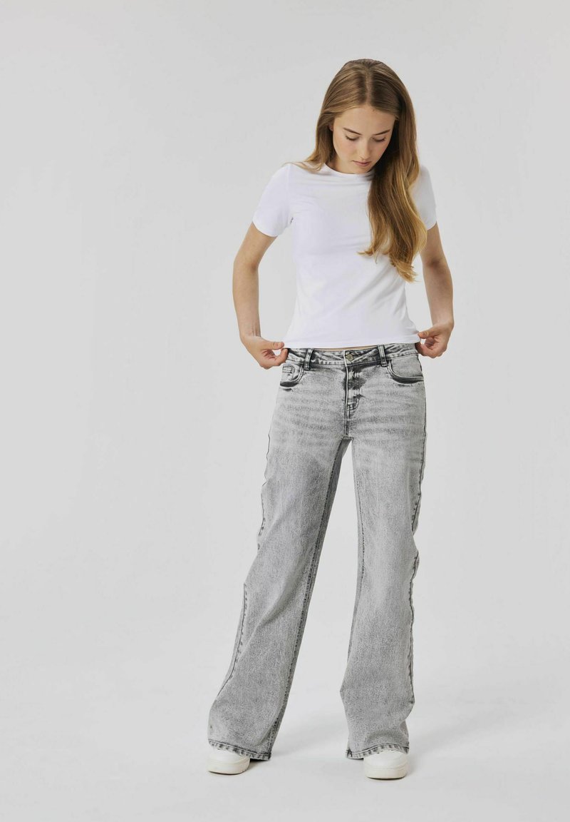 T-shirt bianco a maniche corte abbinato a jeans a gamba larga grigi sbiaditi. L'outfit include semplici sneakers bianche. Tessuti lisci e vestibilità casual.