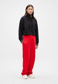 Black cropped sweatshirt with a high collar and zipper, paired with bright red sweatpants, accented by white and black stripes at the cuffs.