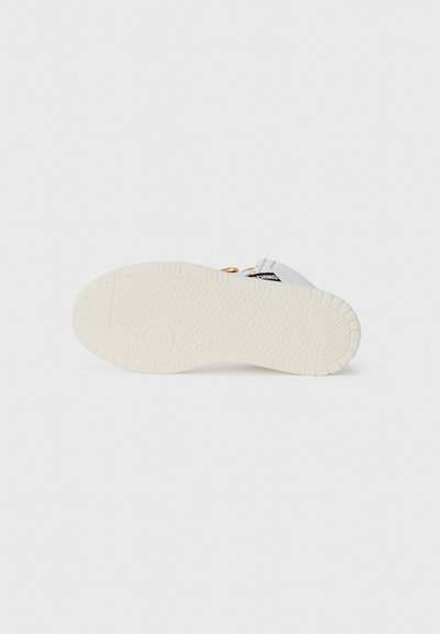 White sneaker sole with textured rubber, featuring a pattern of small dots and grooves for traction. Includes a circular emblem.