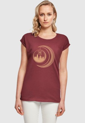 Maron T-shirt med korte ærmer. Har en cremefarvet grafik af en halvmåneform og et ornament med et tårndesign i midten.