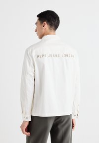 Jachetă albă din bumbac, cu închidere prin butoni și mâneci lungi. "Pepe Jeans London" gravat cu aur pe spate. Croi ajustat.