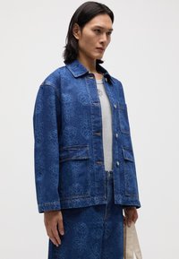 Denimjakke i mørkeblått med blomstermotiv, med krage, to frontlommer og kontrasterende sømmer.