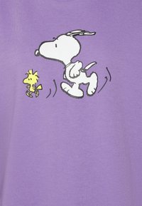 Camisa de algodón morado con una ilustración impresa de un perro blanco y un pájaro amarillo, ambos en una pose juguetona de carrera.
