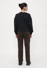 Felpa nera con vestibilità comoda, lunghezza crop e orlo a costine; pantaloni in corduroy marroni con taglio morbido e tasche posteriori discrete; sneakers nere.