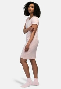Abito corto a maniche corte di colore rosa chiaro con un design aderente, caratterizzato da piccole macchie rosse. Abbinato a calzini alla caviglia morbidi e pelosi di un delicato rosa chiaro.