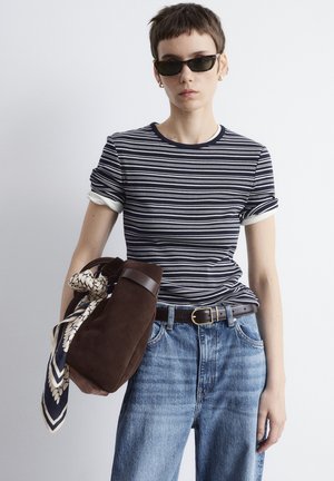 Striped t-shirt with navy and white colors, short sleeves, worn with high-waisted blue jeans. Brown suede bag with a patterned scarf.
