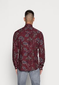 Bordowa koszula na guziki z wzorem liści, długimi rękawami i kołnierzykiem. Charakteryzuje się gładką teksturą i wąskim krojem. Pokazano widok z tyłu.