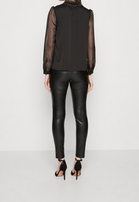 Svart blus med genomskinliga långa ärmar och pärlkrage, i kombination med svarta läderleggings och svarta högklackade skor.