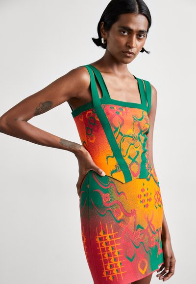 Gebreide jurk met groene banden, met een verloop van oranje en rood met abstracte patronen in groen, waaronder geometrische vormen en lijnen.