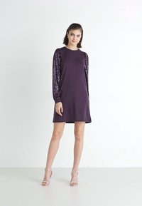Robe violette avec de longues manches en sequins, dotée d'un col rond et d'une coupe droite, fabriquée en tissu doux, longueur genou avec un léger éclat.