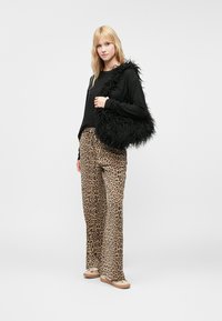 Melnas sintētiskās kažokādas soma, brīvi krīt melns garām piedurknēm tops un bēša leoparda raksta bikses ar izplestenām kājām. Apģērbu papildina brūni slip-on apavi.