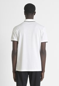 Polo blanco de manga corta, con un borde de collar negro en contraste. Material de algodón suave, diseño sencillo y clásico.