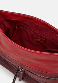 Indvendig i en rød og bordeaux lædertaske med en lynlåslomme, glat overflade og et stoffor, der har minimale brandingdetaljer.