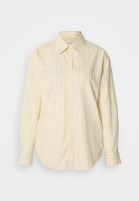 Dzeltens svītrains krekls ar pogām, garām piedurknēm, klasisku apkakli un vienu krūšu kabatu. Svītras zilā krāsā uz mīksta, teksturēta auduma.