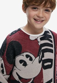 Gebreide trui met een rode achtergrond en een groot zwart-wit Mickey Mouse graphic, met witte accenten rond de kraag.