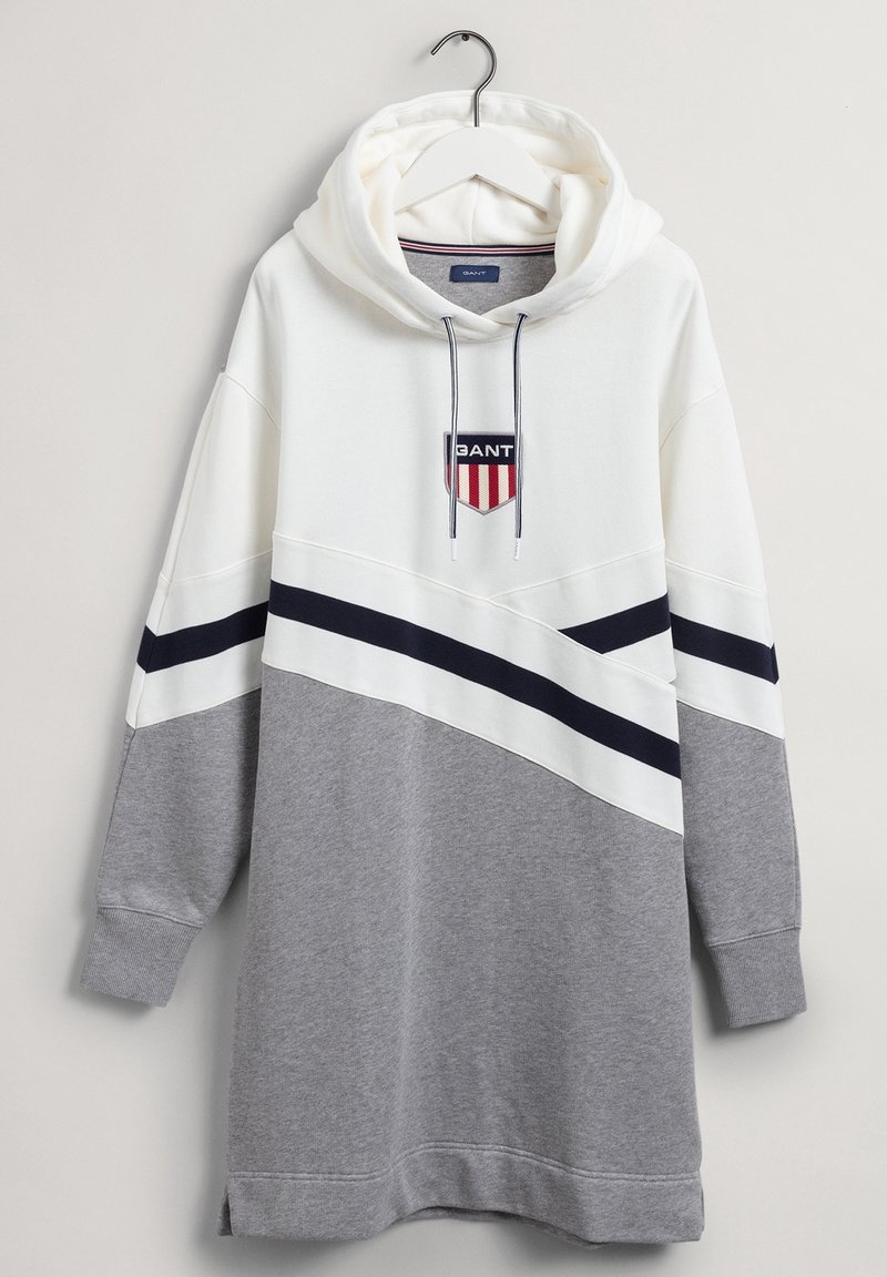Robe à capuche manches longues avec blocs de couleurs blanc et gris, rayures diagonales bleu marine, écusson logo devant et capuche à cordon sur un cintre.