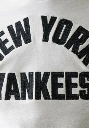 Testo nero ricamato "NEW YORK YANKEES" su sfondo di tessuto bianco, centrato e disposto in un design ad arco e linea retta.