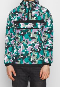 Kleurrijk camouflagejack met capuchon, met groen, paars en zwarte patronen, een voorzak en elastische manchetten. Logo zichtbaar op de borst.