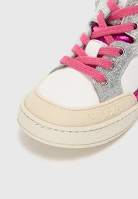 Weiße Sneaker mit einer strukturierten cremefarbenen Sohle, silbernen Glitzerakzenten, pinken Schnürsenkeln und einem glänzenden pinken Panel an der Seite. "POM DAPI" auf der Sohle gedruckt.