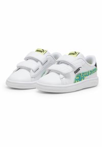 Baskets blanches avec des bandes Velcro, arborant une rayure verte à motif et des accents noirs au niveau du talon. Semelle en caoutchouc avec logo sur le côté.