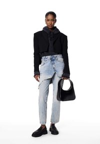 Afkortet sort blazer over en grå hættetrøje, kombineret med slidte lyseblå jeans og sorte platåsko, holder en sort håndtaske.