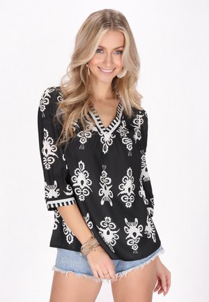 Blusa nera con motivi floreali bianchi, scollo a V e maniche a tre quarti. Presenta dettagli a righe sulle maniche e un tessuto leggero.