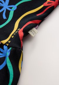Tissu noir avec des lignes ondulées colorées et des motifs floraux en bleu, vert, rouge et jaune, avec une petite étiquette blanche portant la mention « little bird ».