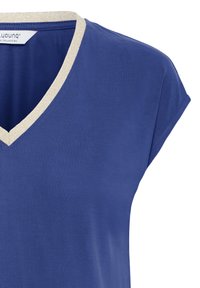 Chemise bleue à manches courtes avec col en V bordé de beige, en tissu doux, montrant les détails du haut devant et des manches.